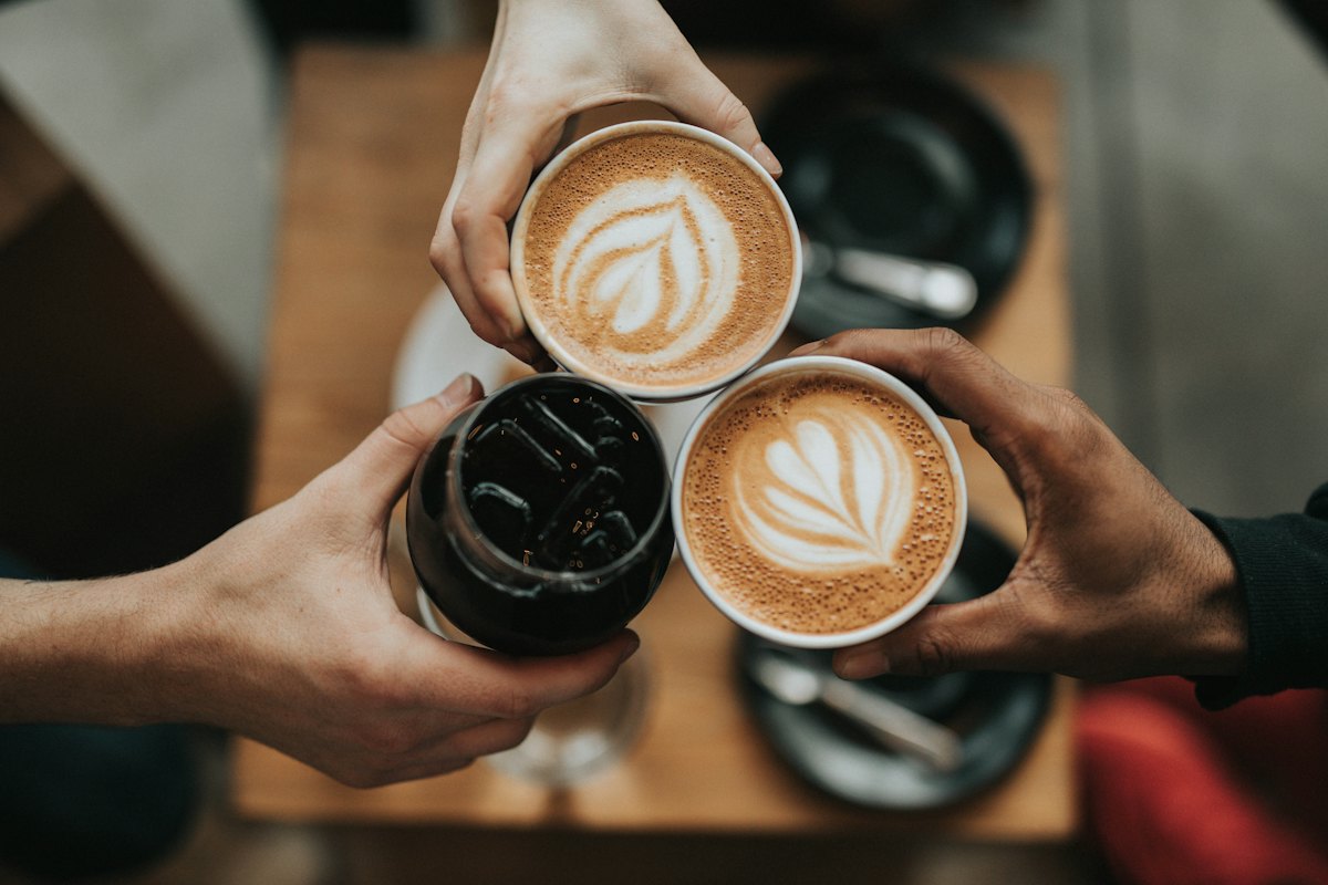 Ahşap masa üzerinde latte fincanları tokuşturan eller